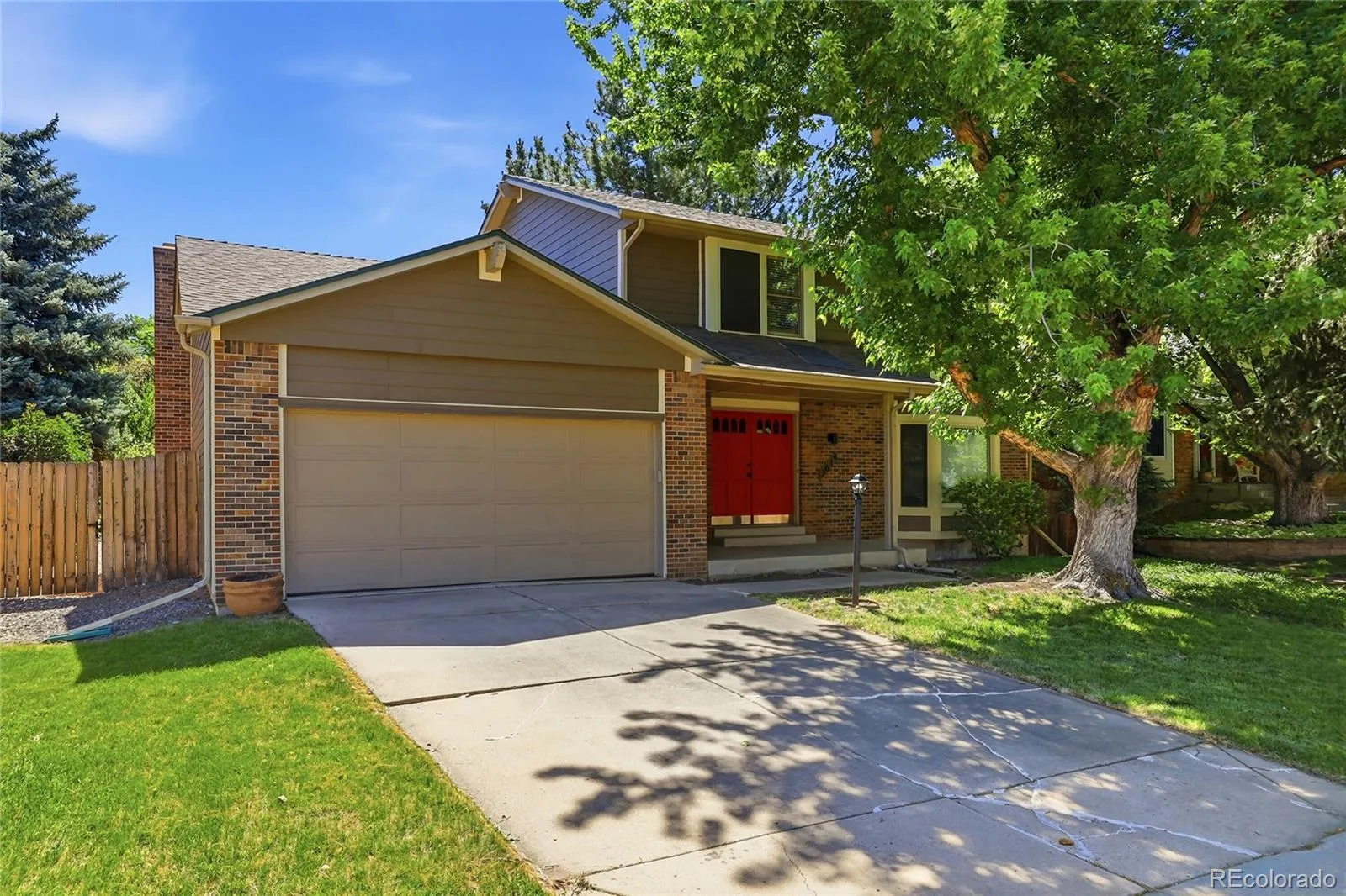 Two-story brick and siding home with red double doors beneath a mature shade tree in Centennial, Colorado